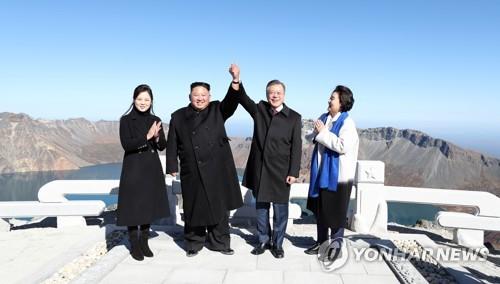 South Korean President Moon Jae-in (2nd from R) and North Korean leader Kim Jong-un raise each other's hand atop the North's Mount Paekdu on Sept. 20, 2018, as their wives, South Korean first lady Kim Jung-sook (R) and her North Korean counterpart Ri Sol-ju applaud. (Yonhap)