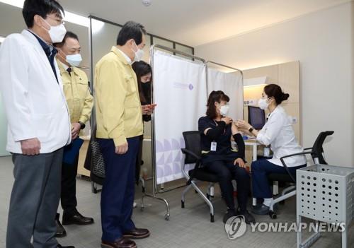 Chung Mi-kyeong (2nd from R), a sanitation worker of the National Medical Center, receives a Pfizer vaccine at the hospital in central Seoul on Feb. 27, 2021, while Prime Minister Chung Sye-kyun (3rd from L) looks on. She became the first South Korean to get the Pfizer product. (Yonhap)