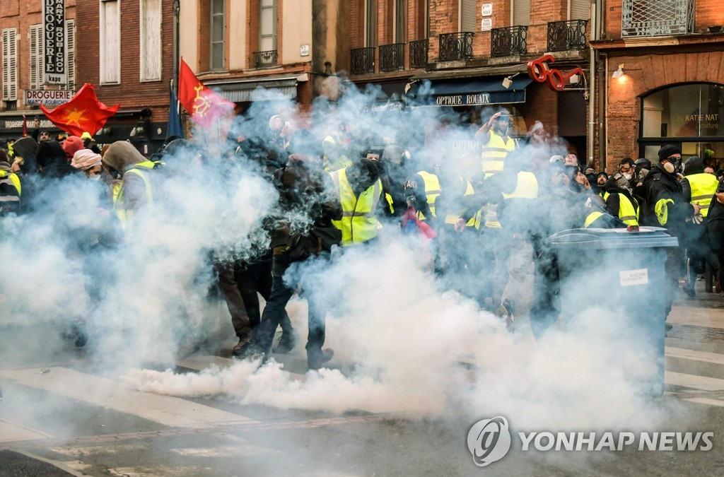 5일(현지시간) 프랑스 툴루스에서 열린 '노란 조끼' 시위 중 시위대가 경찰이 쏜 최루탄에서 연기가 나오는 가운데 서 있다 [AFP=연합뉴스]