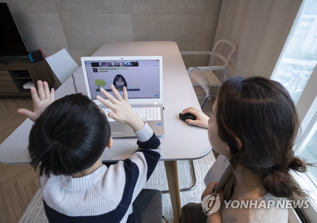 A student in the first year of elementary school takes online classes at his home in the Seoul ward of Yongsan with the help of his mother on April 20, 2020. (Yonhap)