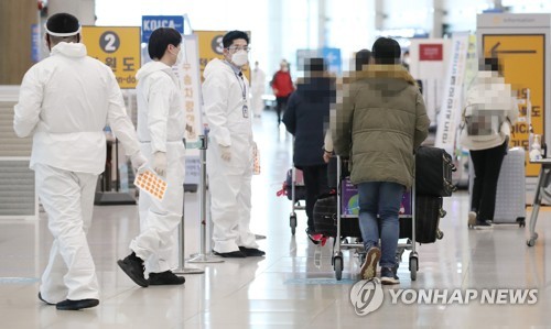 This photo taken on Jan. 19, 2021, shows health workers clad in protective suits guiding arrivals at Incheon International Airport in Incheon. (Yonhap)