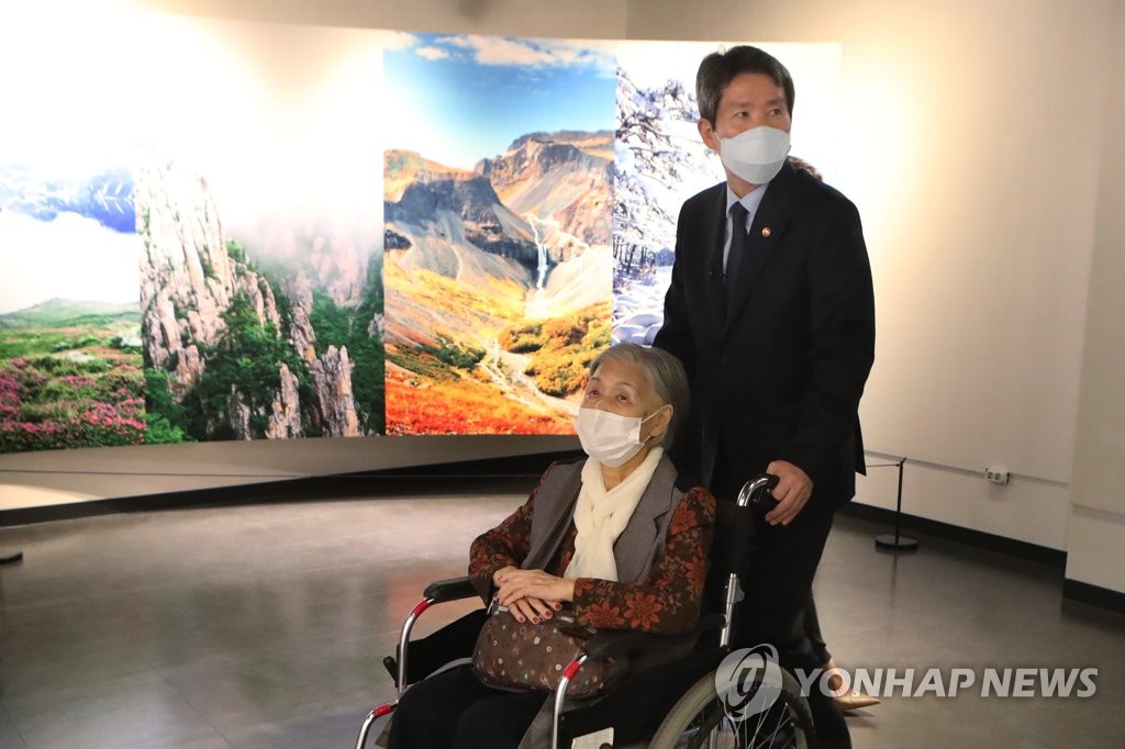Unification Minister Lee In-young (R) pushes the wheelchair of a separated family member during a photo exhibition on North Korea held at Odusan Unification Observatory in Paju, just south of the demilitarized zone, on Oct. 7, 2021. (Yonhap)