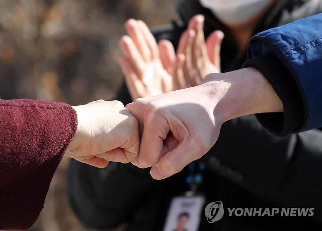 资料图片：治愈并解除隔离的新冠患者（右）在离开生活治疗中心前与医务人员击拳告别。 韩联社
