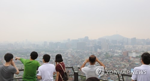This May 2017 file photo shows people looking at the landscape of downtown Seoul on the slope of the city's Mount Nam as the city is covered in a thick haze caused by fine dust. (Yonhap)