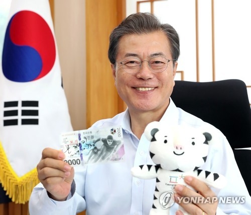 This photo provided by the presidential office Cheong Wa Dae shows President Moon Jae-in holding up a commemorative banknote and one of the mascots for the 2018 PyeongChang Winter Olympic Games in his office on Oct. 13, 2017. (Yonhap)