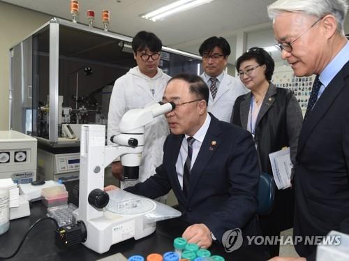 Hong Nam-ki, the minister of economy and finance, looks through a microscope in a laboratory at a bio-health company in Pangyo, just south of Seoul on Feb. 27, 2019. This photo was provided by the Ministry of Economy and Finance. (Yonhap)