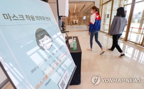 Customers pass by a signboard on a mask mandate at the entrance of a department store in Seoul on April 11, 2021. (Yonhap)