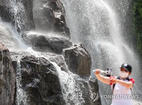 A citizen tries to beat the scorching heat wave at an artificial waterfall in eastern Seoul on July 24, 2021. (Yonhap)