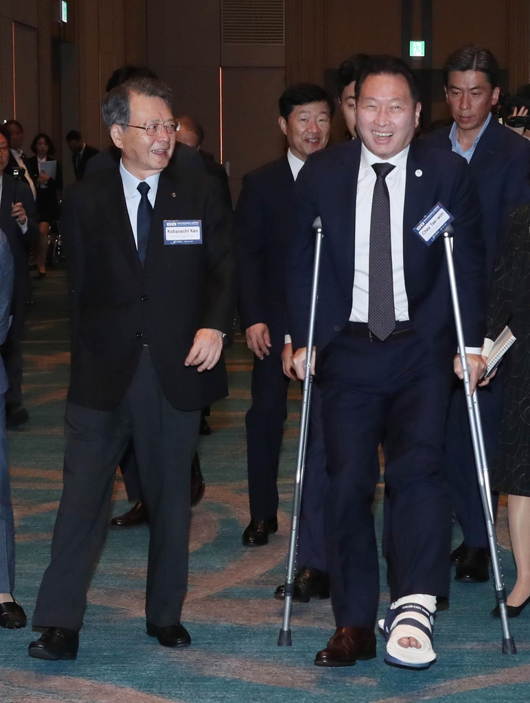 SK Group Chairman Chey Tae-won (R), who doubles as the chair of the Korea Chamber of Commerce and Industry (KCCI), smiles as he appears, wearing a cast after a leg injury, at the 12th chairs' meeting between the KCCI and the Japan Chamber of Commerce and Industry (JCCI), in Busan, on June 9, 2023. Walking alongside Chey is Ken Kobayashi, chairperson of the JCCI. (PHOTO NOT FOR SALE) (Yonhap)