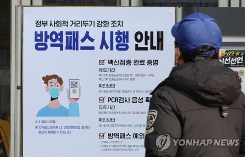 Une personne regarde un panneau présentant le système de passe vaccinal installé devant une grande surface à Séoul le lundi 10 janvier 2022. 