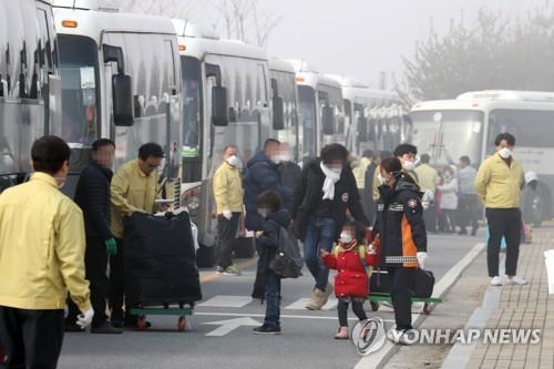 政府が用意したバスに乗り込む帰国者たち＝１５日、鎮川（聯合ニュース）