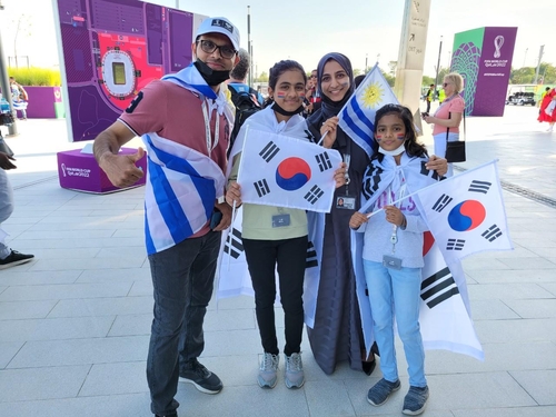 Una familia india de cuatro miembros posa ante la cámara, el 24 de noviembre de 2022 (hora local), con las banderas de Corea del Sur y Uruguay antes del partido entre los dos países, en el estadio de la Ciudad de la Educación, en la ciudad de Rayán, al oeste de Doha. 