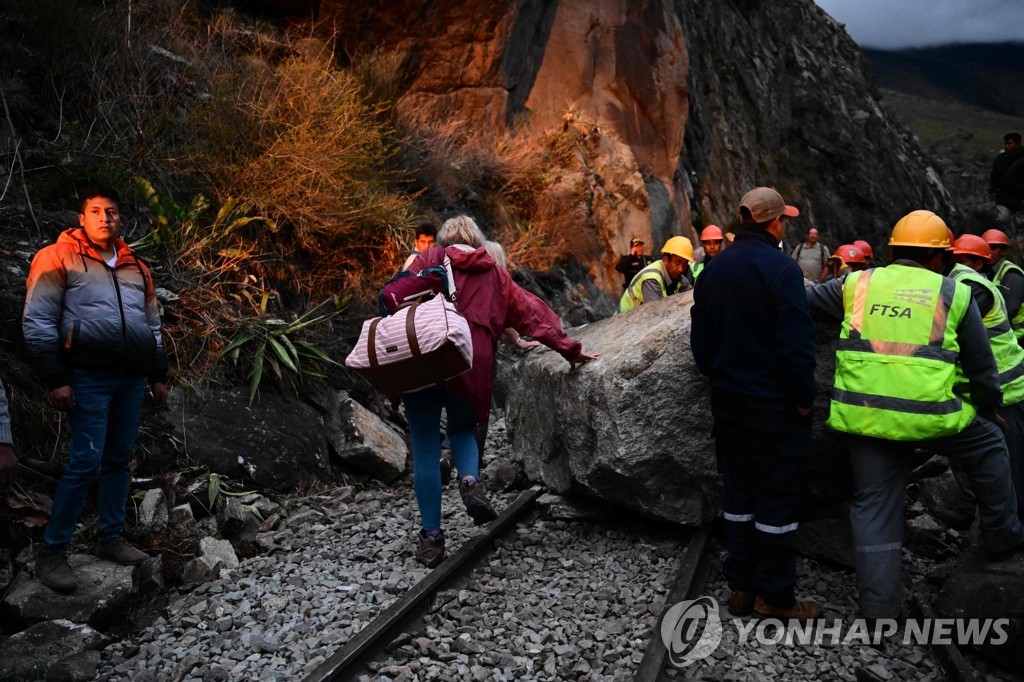 Tourists in Machu Picchu walking along rock-damaged railroad tracks