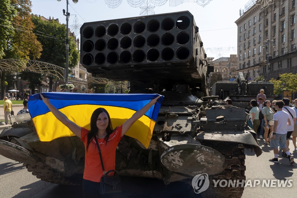 21일 러시아군 군용 차량 앞에서 우크라이나 국기를 펼쳐 든 한 여성.