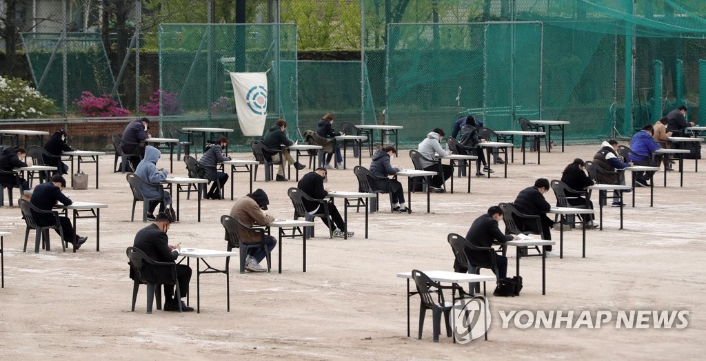 Applicants for an insurance sales license take a test, postponed due to the coronavirus outbreak, on the athletics field of Myeonggi College campus in Seoul on April 25, 2020. (Yonhap)