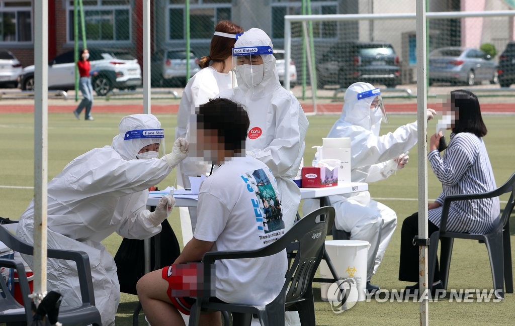 This photo taken on May 13, 2021, and provided by Inje County shows medical workers collecting specimen from students at a makeshift coronavirus testing facility at a high school in Inje, Gangwon Province. (Yonhap)