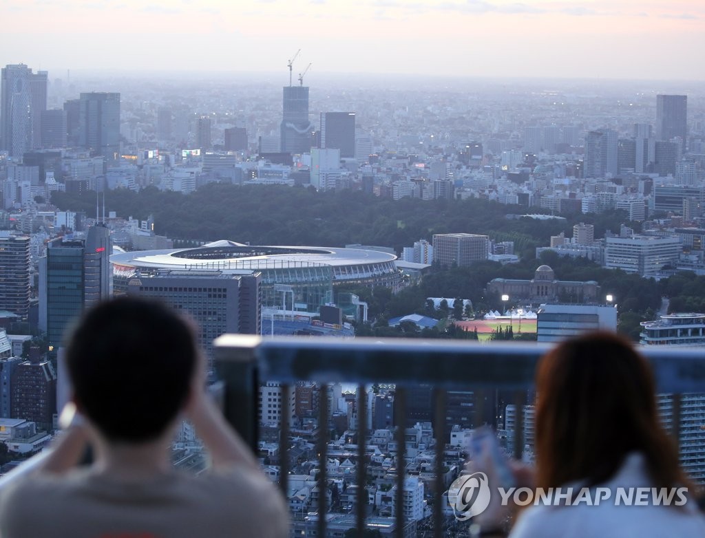 A Japanese citizen takes a photo of the National Stadium, the venue for the opening and closing ceremonies of the Tokyo Olympics, from the top of a building in Tokyo on July 18, 2021. (Yonhap)