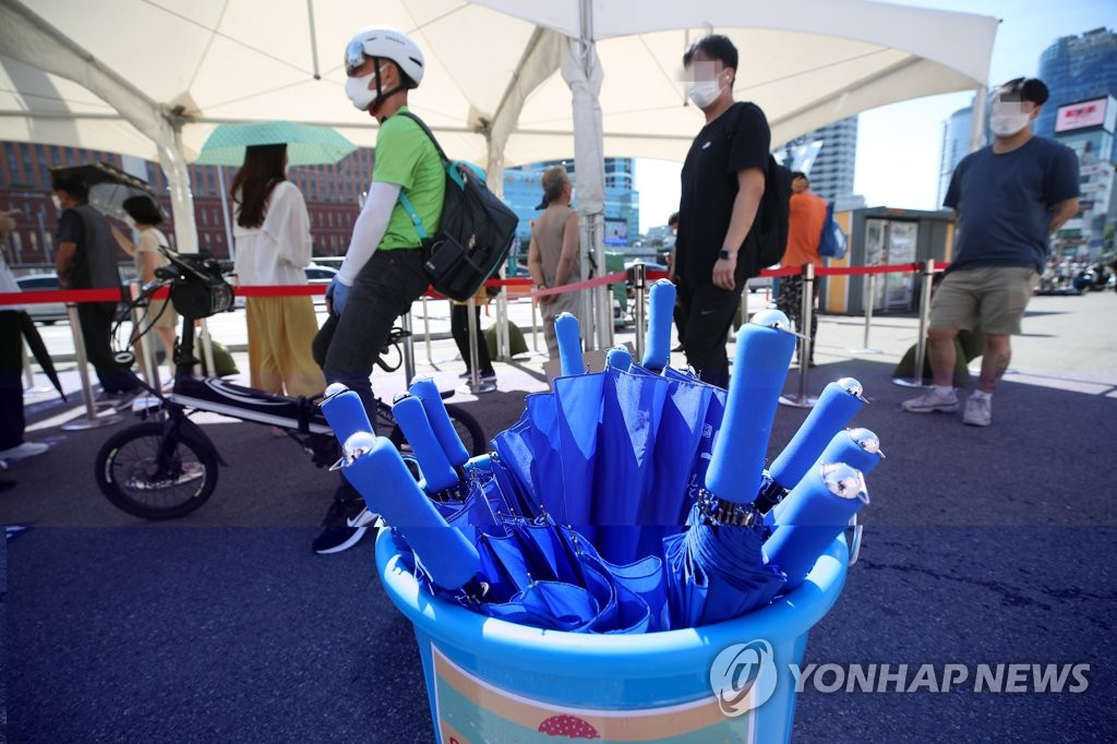 People line up to take coronavirus tests at a makeshift testing facility in front of Seoul Station in central Seoul on July 25, 2021, with parasols available for them to block the sunlight. (Yonhap)
