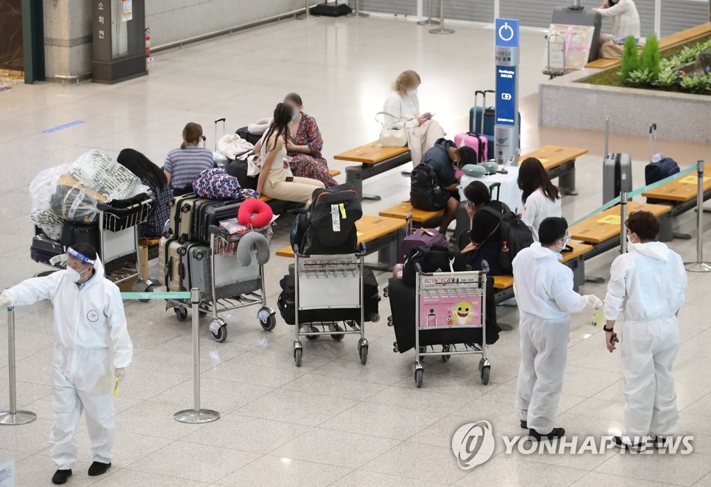 Health workers in protective suits guide travelers at Incheon International Airport, west of Seoul, on Aug. 4, 2021. (Yonhap)