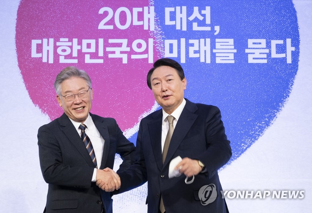 This file photo from Nov. 24, 2021, shows Lee Jae-myung (L) and Yoon Suk-yeol, presidential nominees of the ruling and main opposition parties, respectively, shaking hands at a forum in Seoul. (Yonhap) 