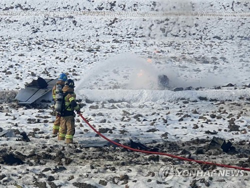 Firefighters pour water onto the site of a warplane crash in Hoengseong County, about 140 kilometers east of Seoul, on Dec. 26, 2022, in this photo released by the fire service in the county. (PHOTO NOT FOR SALE) (Yonhap)