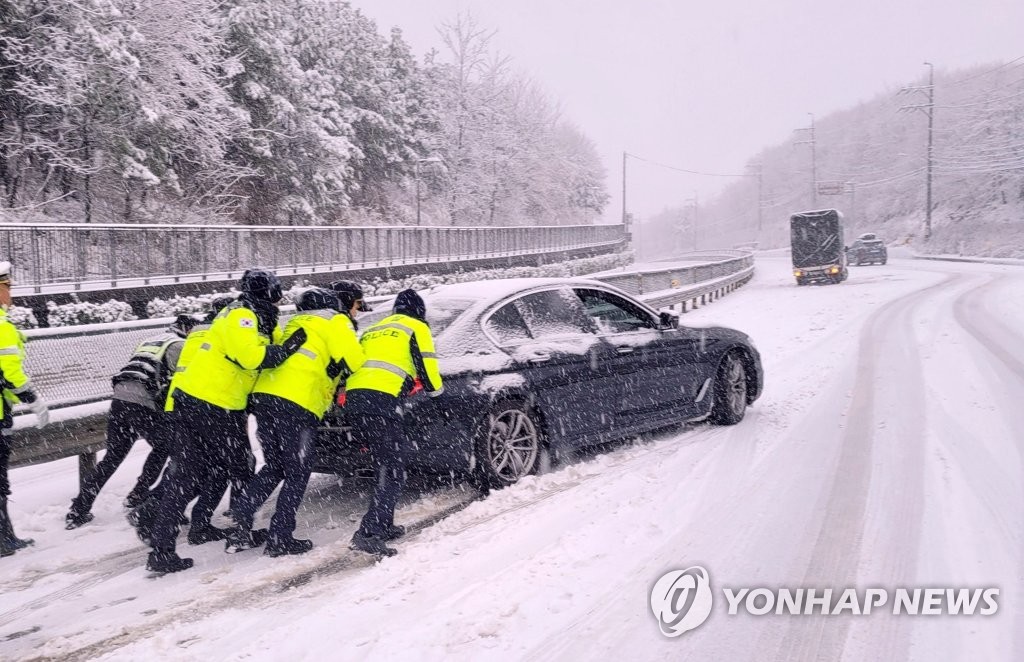 Des policiers poussent une voiture sur une route enneigée du comté de Yangyang, le dimanche 15 janvier 2023. (Photo fournie par l'Agence de la police provinciale du Gangwon. Revente et archivage interdits)