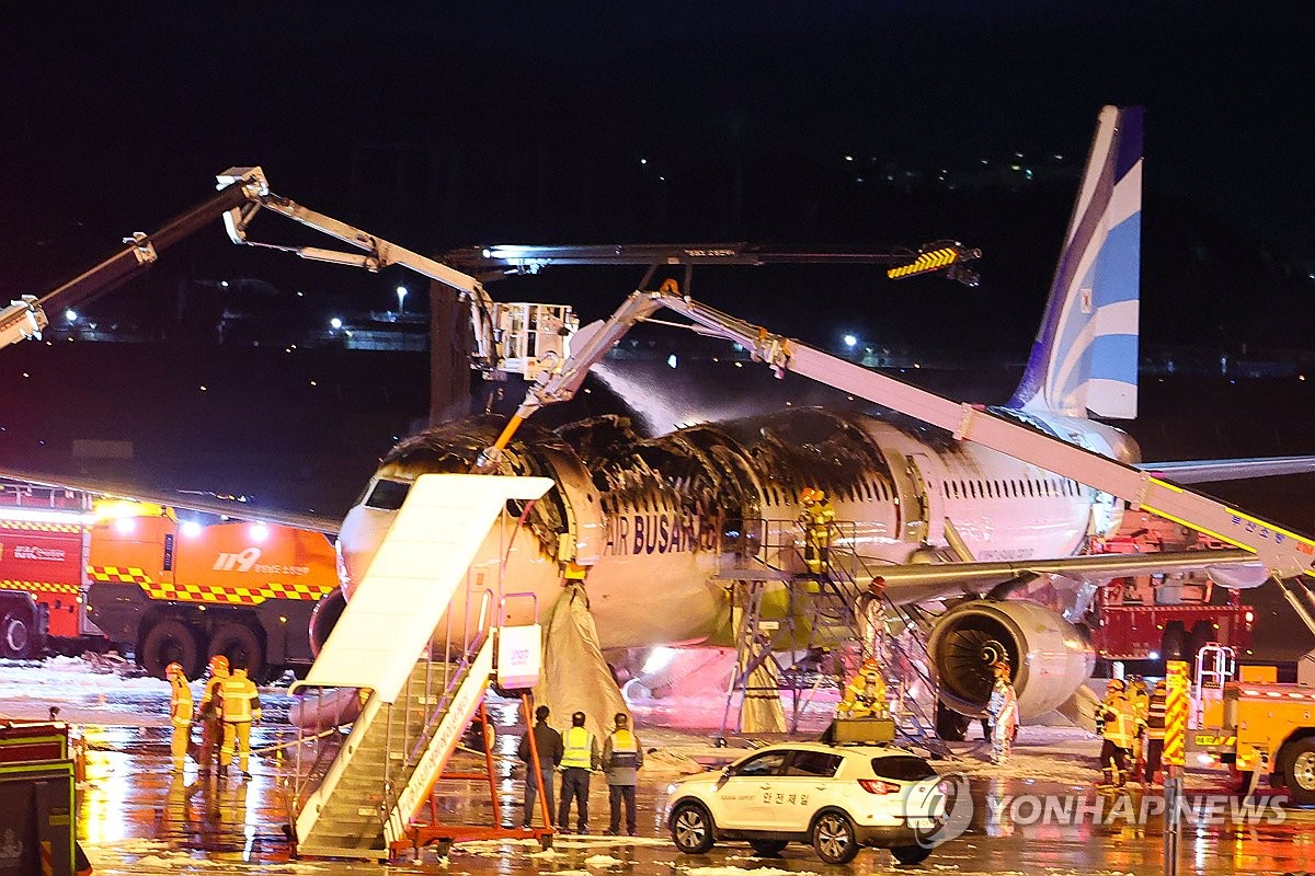 Los bomberos verifican un avión de Busan dañado después de un incendio en el aeropuerto internacional de Gimhae en Busan, a 320 kilómetros al sureste de Seúl, el 28 de enero de 2025. (Yonhap)